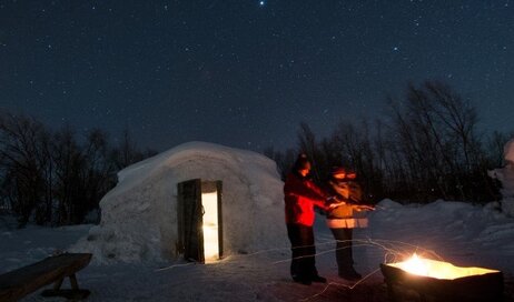 A couple in a snow igloo by a fire
